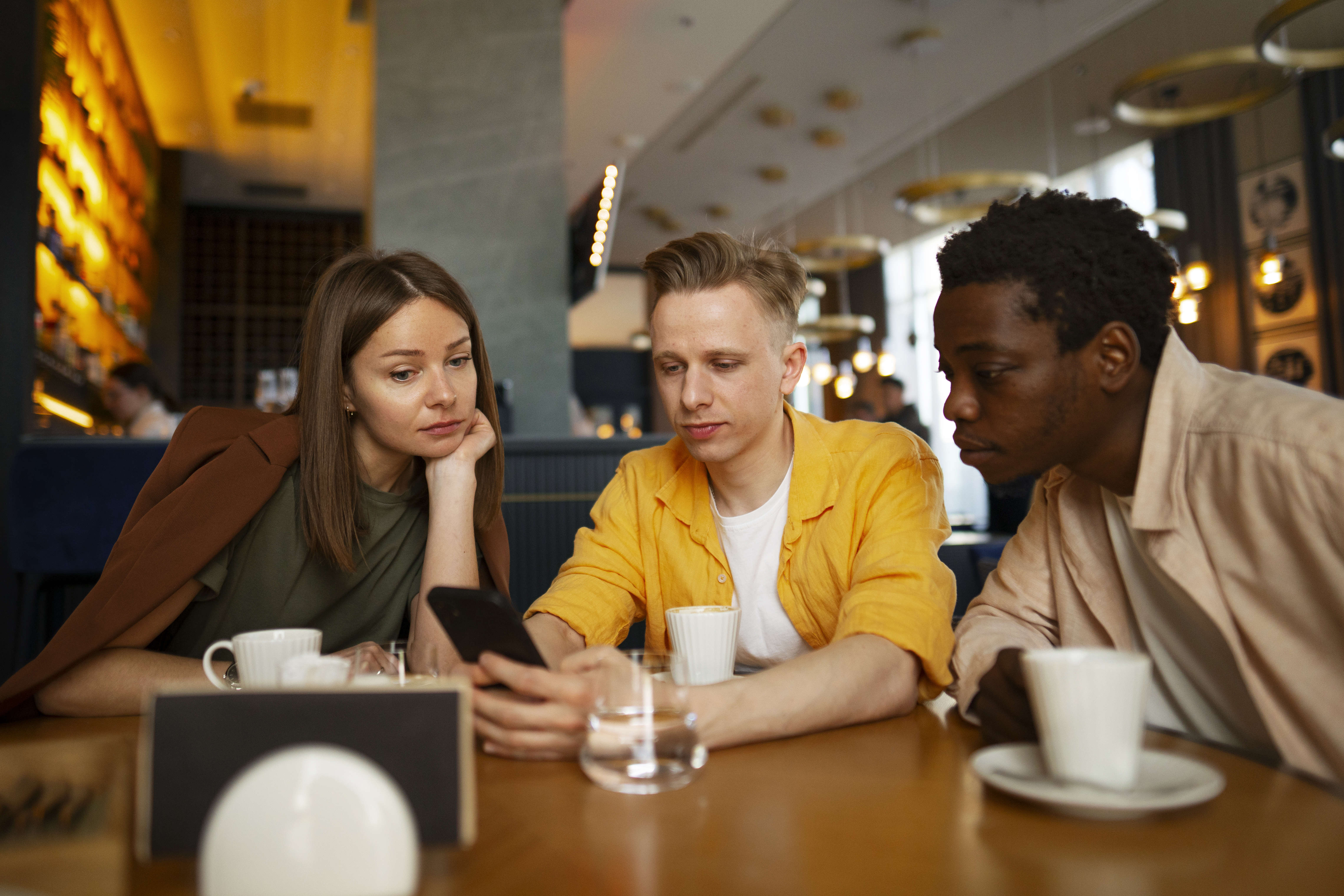 a photo of three diners gathered around a phone while sitting at a café table.